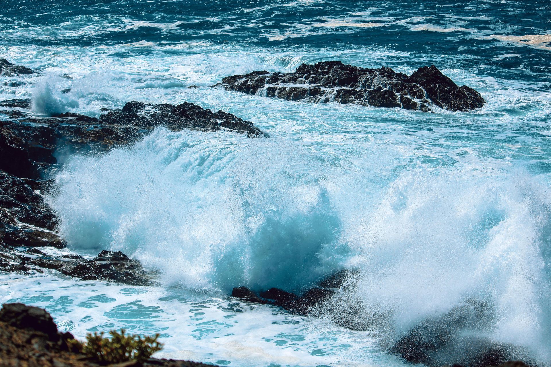 Waves crash against dark rocks in a turquoise ocean, creating white spray.