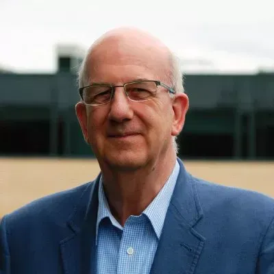 Man with glasses wearing a blue blazer and light blue shirt, outside a building.