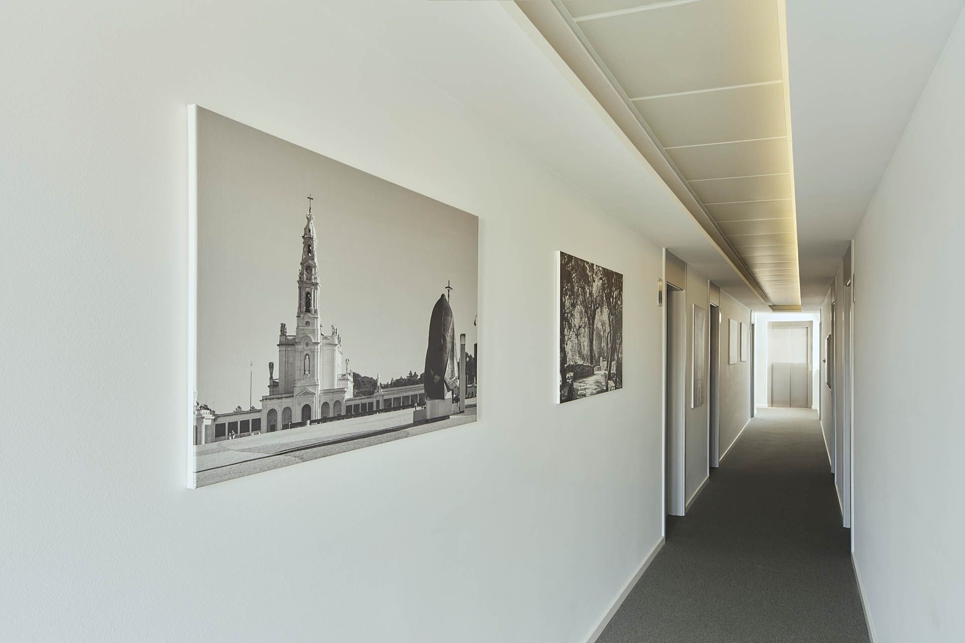 Corredor minimalista com fotos da cidade em preto e branco em paredes brancas e luz brilhante ao fundo.