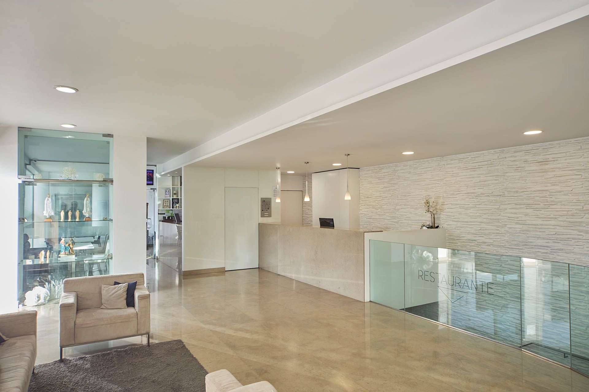 Sala de estar moderna de conceito aberto com guarda-corpo de vidro, piso de madeira clara e parede com detalhes em mármore.