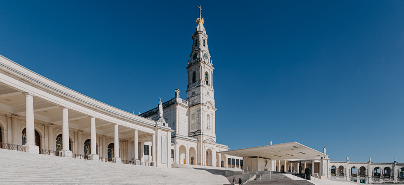 Pátio da grande mesquita com arcadas brancas e um minarete alto sob um céu azul claro.