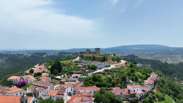 Castelo no topo da colina com vista para uma aldeia de telhados vermelhos e um vale verdejante sob um céu límpido.