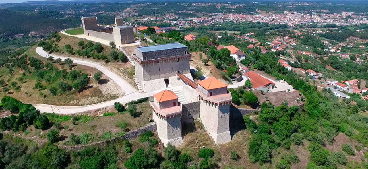Vista aérea de uma fortaleza de pedra em uma colina acima de um vale verdejante e da cidade.