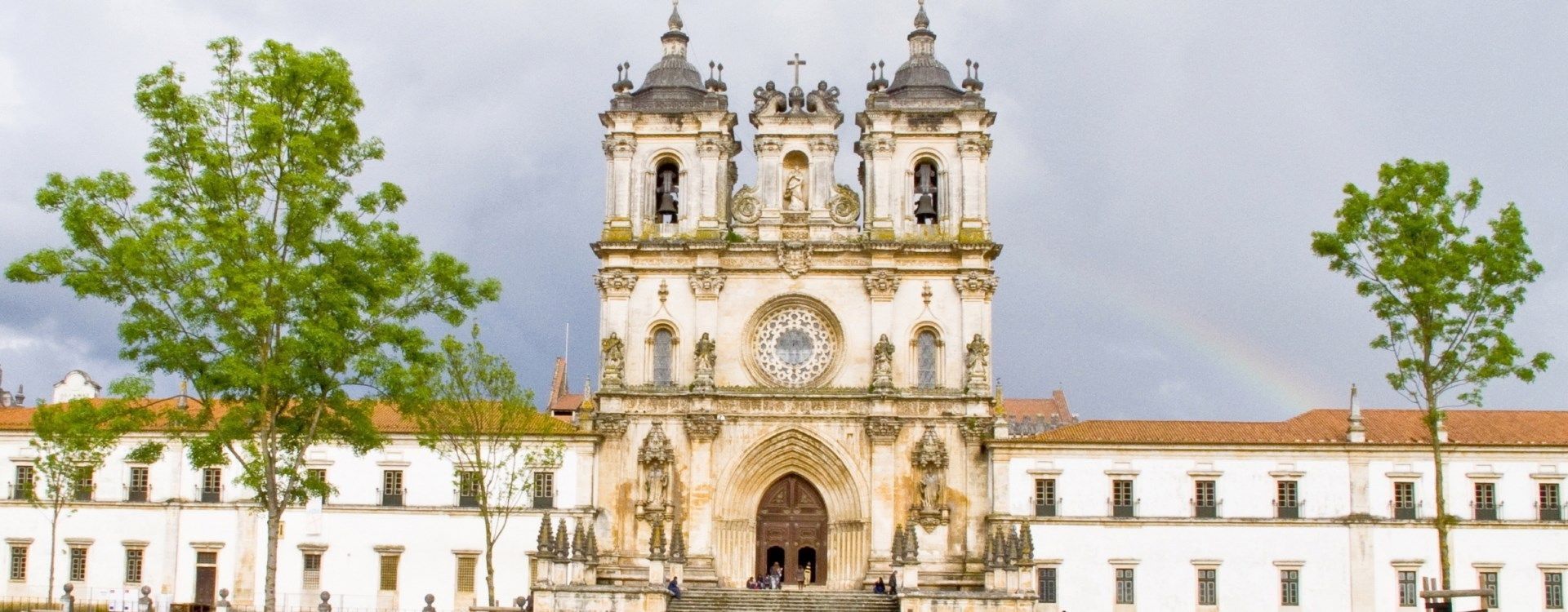 Igreja histórica branca com duas torres sineiras e árvores em frente, sob um céu claro.