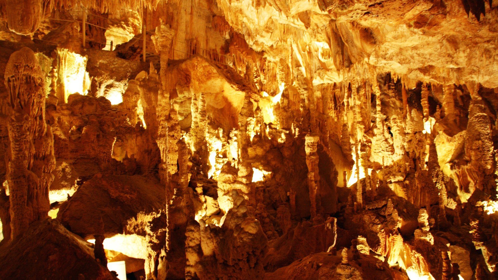 Interior de caverna iluminado com estalactites e formações rochosas em tons de laranja brilhante.