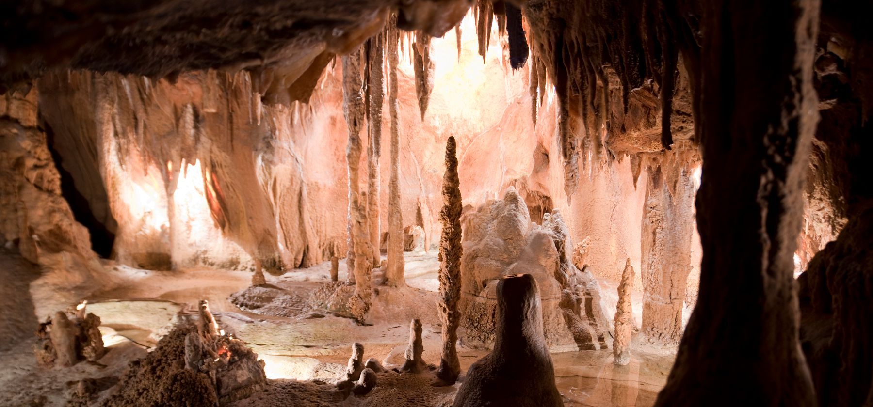 Uma caverna de calcário com iluminação quente, repleta de estalactites, estalagmites e piso rochoso.