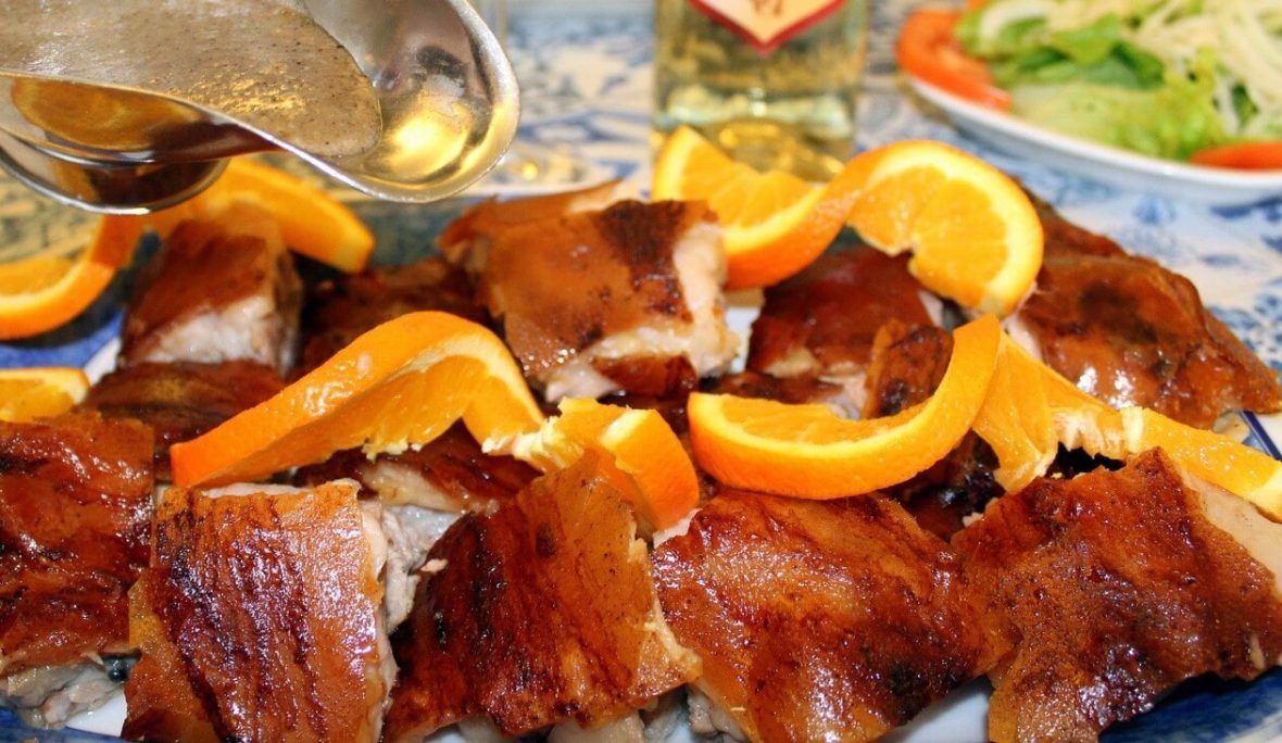 Carne assada com molho e decorada com fatias de laranja, servida em uma travessa.