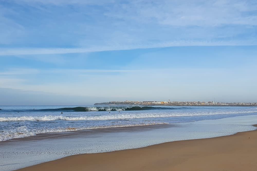 Praia de areia com ondas suaves sob um céu azul límpido.