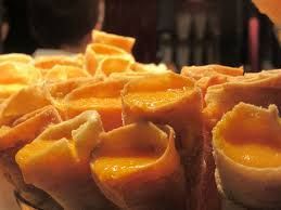 Fileiras de doces ou sobremesas laranja em formato de taça, com recheio brilhante, dispostas em uma bandeja.