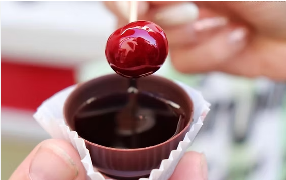 Balas de cereja vermelha mergulhadas em chocolate amargo derretido, dentro de uma pequena embalagem.