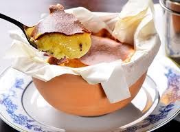 Sobremesa servida em uma tigela laranja com guardanapo branco, coberta com uma colherada de bolo ou creme e cacau em pó.