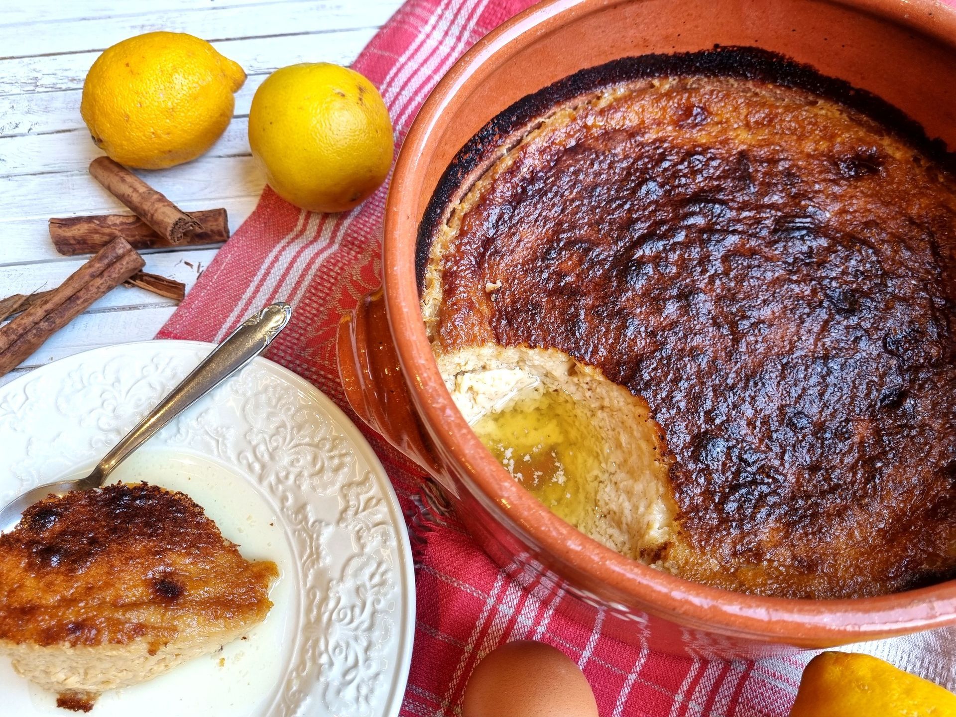 Tarte de sobremesa servida numa travessa de terracota com limões, paus de canela e uma fatia num prato.