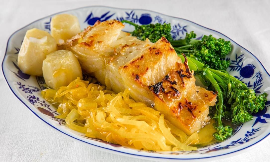 Peixe assado servido com batatas, repolho e brócolis em um prato decorado.