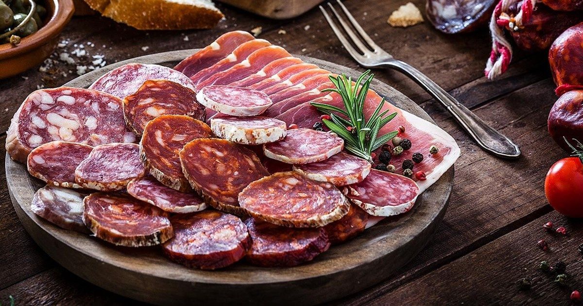 Fatias variadas de carnes curadas dispostas em uma travessa com salsa sobre uma mesa rústica.