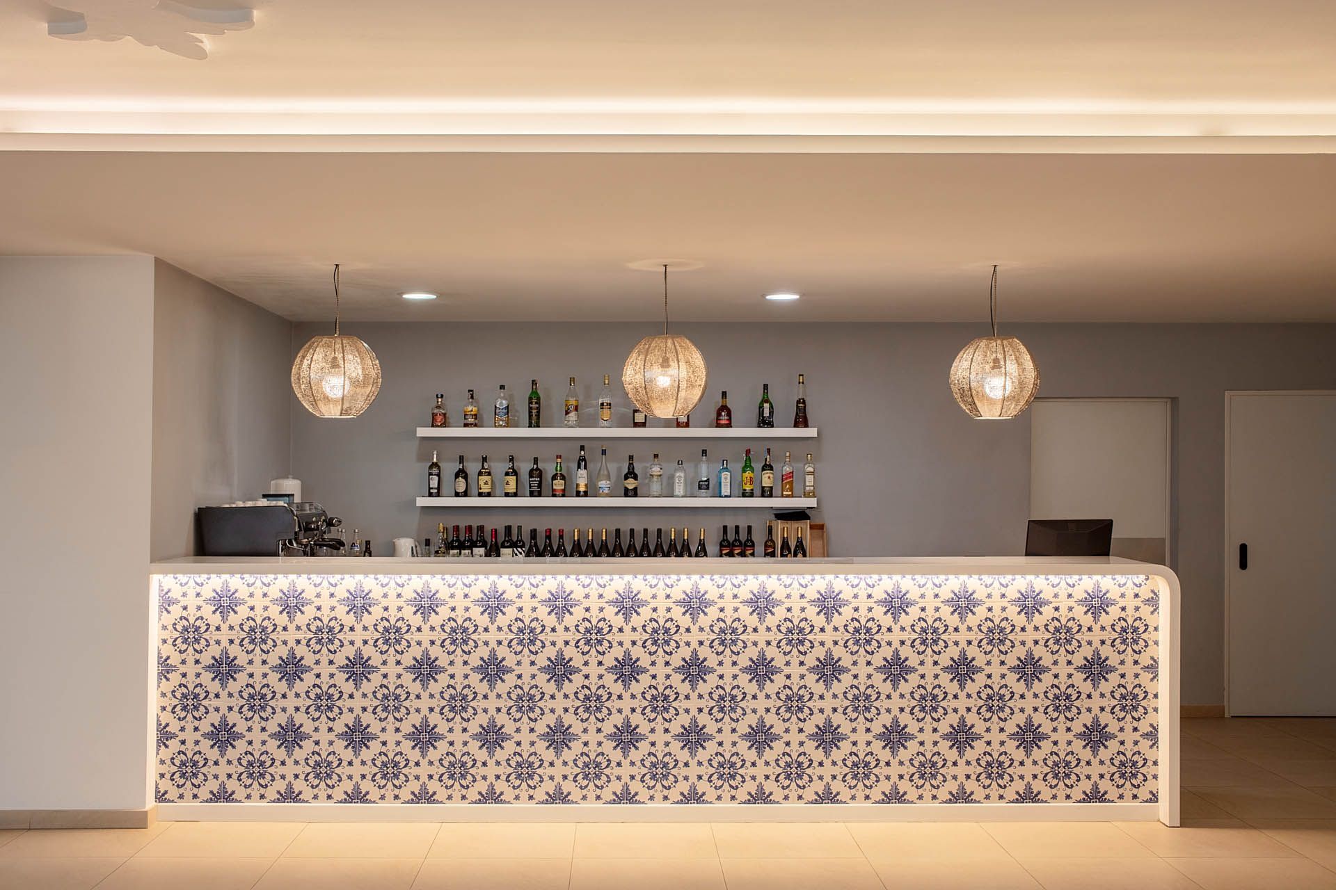 Bar moderno com frente estampada, garrafas em prateleiras e três luminárias pendentes.