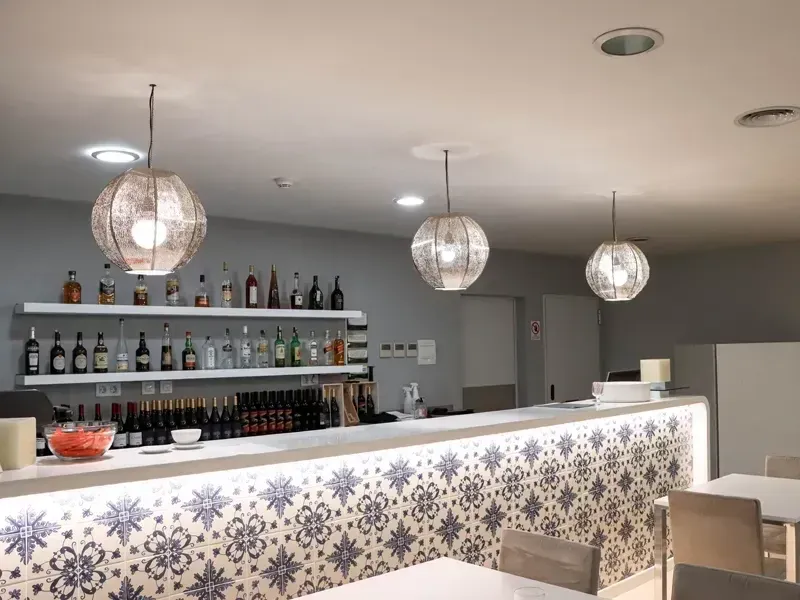 Interior de bar moderno com luminárias pendentes, balcão estampado e prateleiras de garrafas.