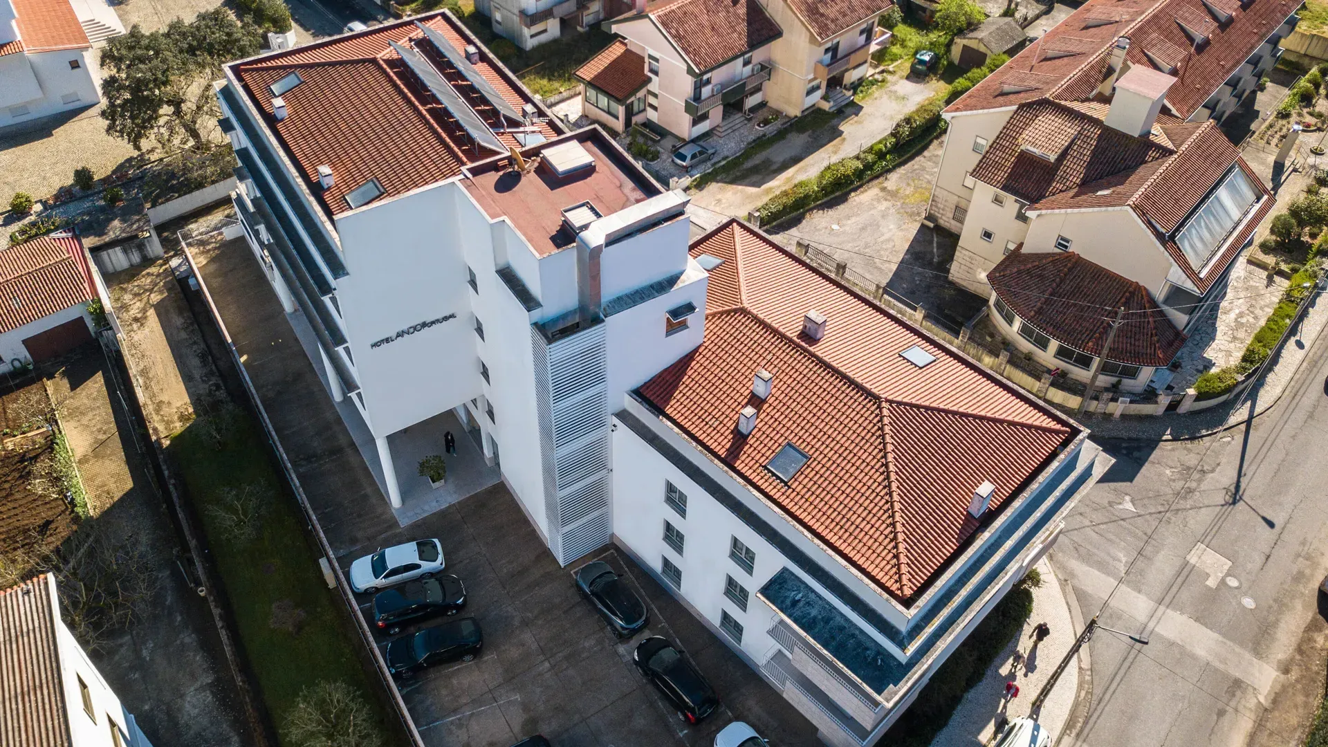 Vista aérea de prédios de apartamentos brancos com telhados de telha vermelha ao longo de uma rua tranquila em um bairro residencial.