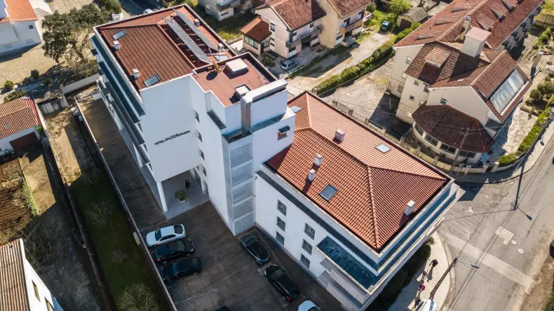 Vista aérea de prédios de apartamentos brancos com telhados de telha vermelha ao longo de uma rua tranquila em um bairro residencial.