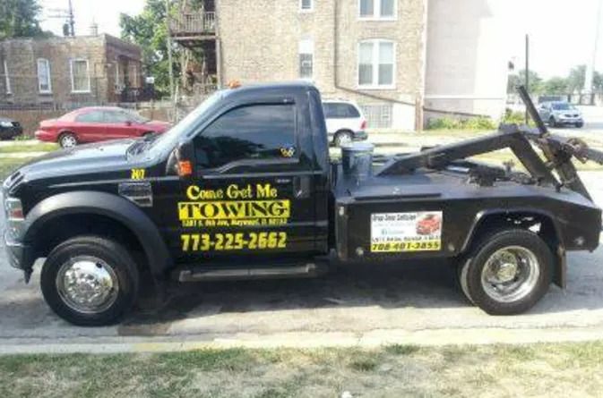 Black tow truck with yellow lettering parked on a street in front of houses