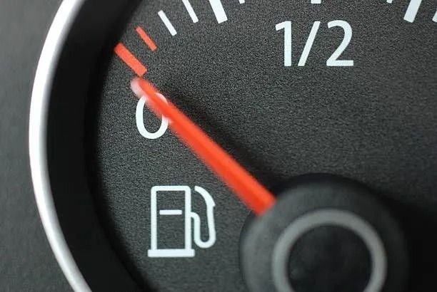 Fuel gauge showing low tank near empty, with red needle and gas pump icon.