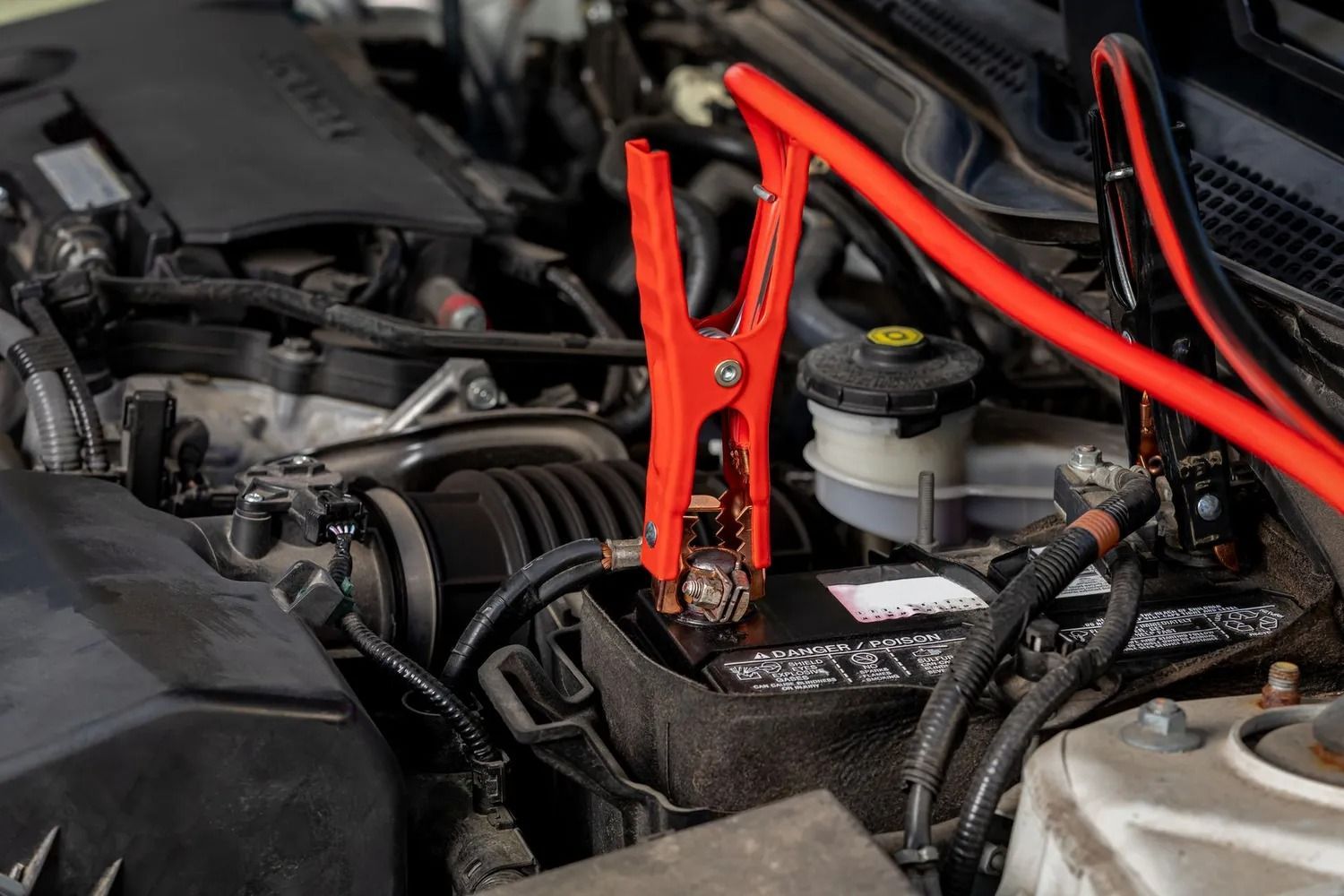 Red jumper cables attached to a car battery in an engine bay.