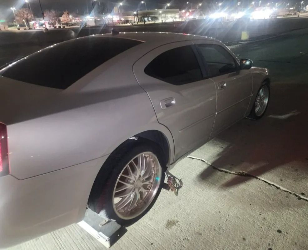 Silver sedan with a rear wheel immobilized by a wheel boot at night in a parking lot