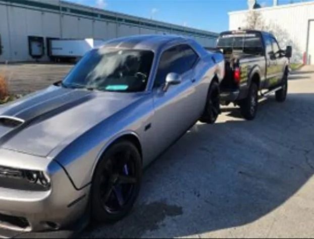 Gray Dodge Challenger towing a black pickup truck on a trailer in an industrial lot