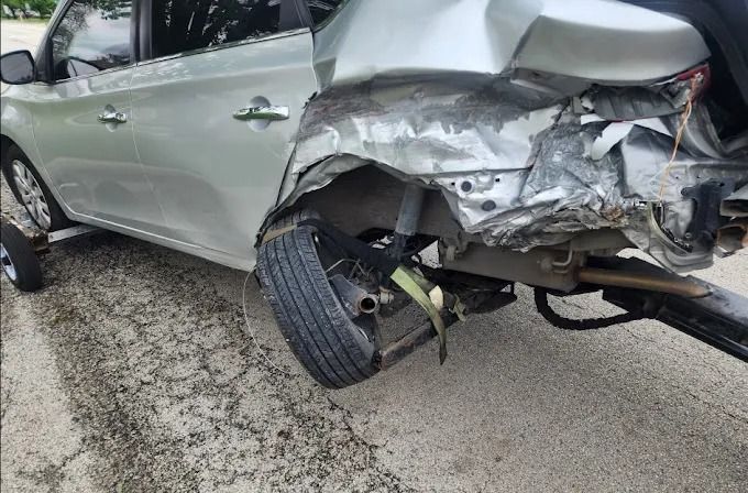 Silver SUV with severe rear-end damage on a road, rear wheel detached and body crumpled