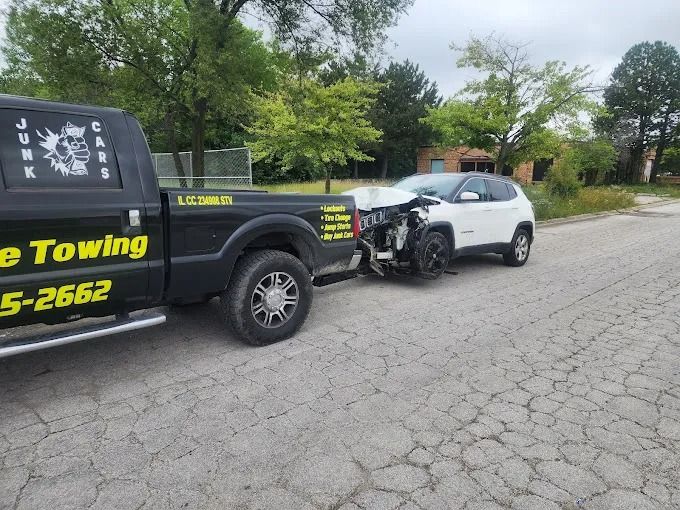 Tow truck towing a white SUV with front-end damage on a cracked roadside