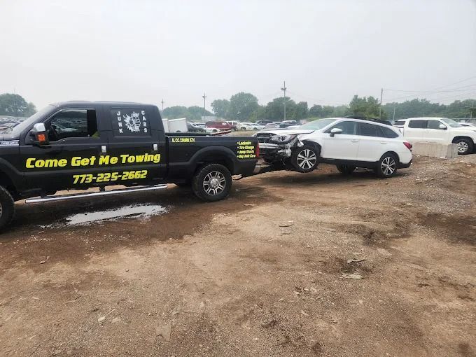 Tow truck towing a white SUV from a muddy roadside lot under an overcast sky