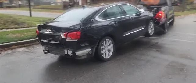 Two cars involved in a rear-end collision on a rainy street, black sedan hit from behind by a red car.