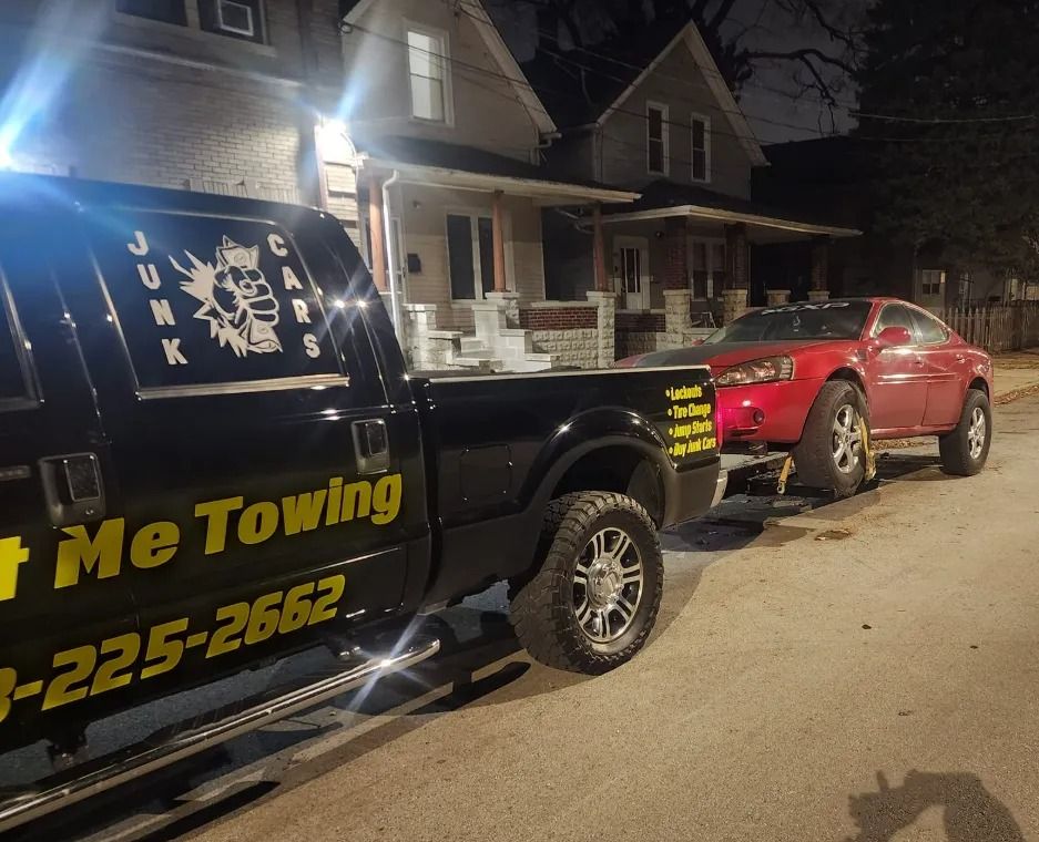 Tow truck towing a red car on a residential street at night, with lit house in background