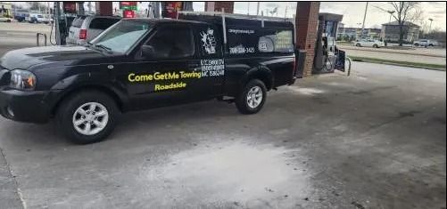 Black pickup truck with yellow lettering parked at a gas station pump under a canopy