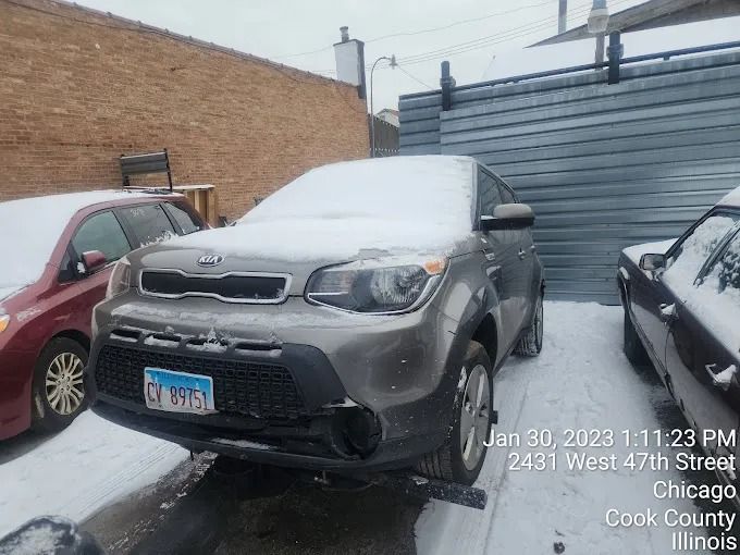 Snow-covered gray SUV parked in an alley beside brick buildings in Chicago