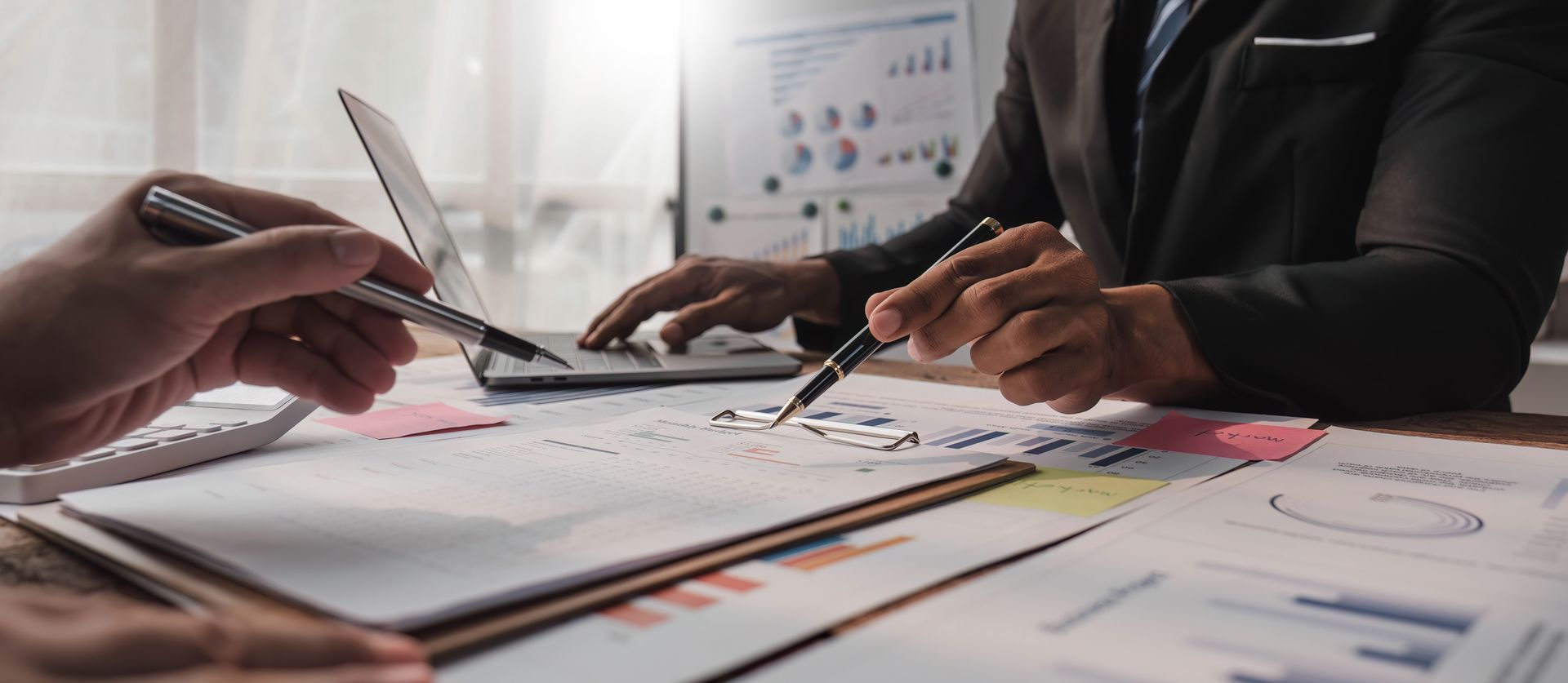 Hands working over financial charts and papers with a pen and calculator on a desk