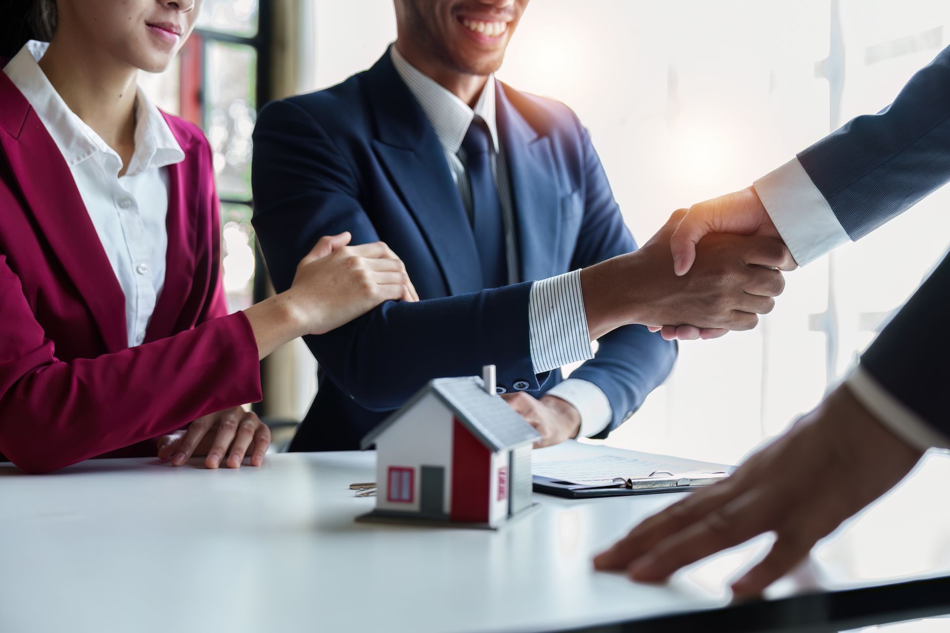 Businesspeople shaking hands over a table with a small model house in the foreground
