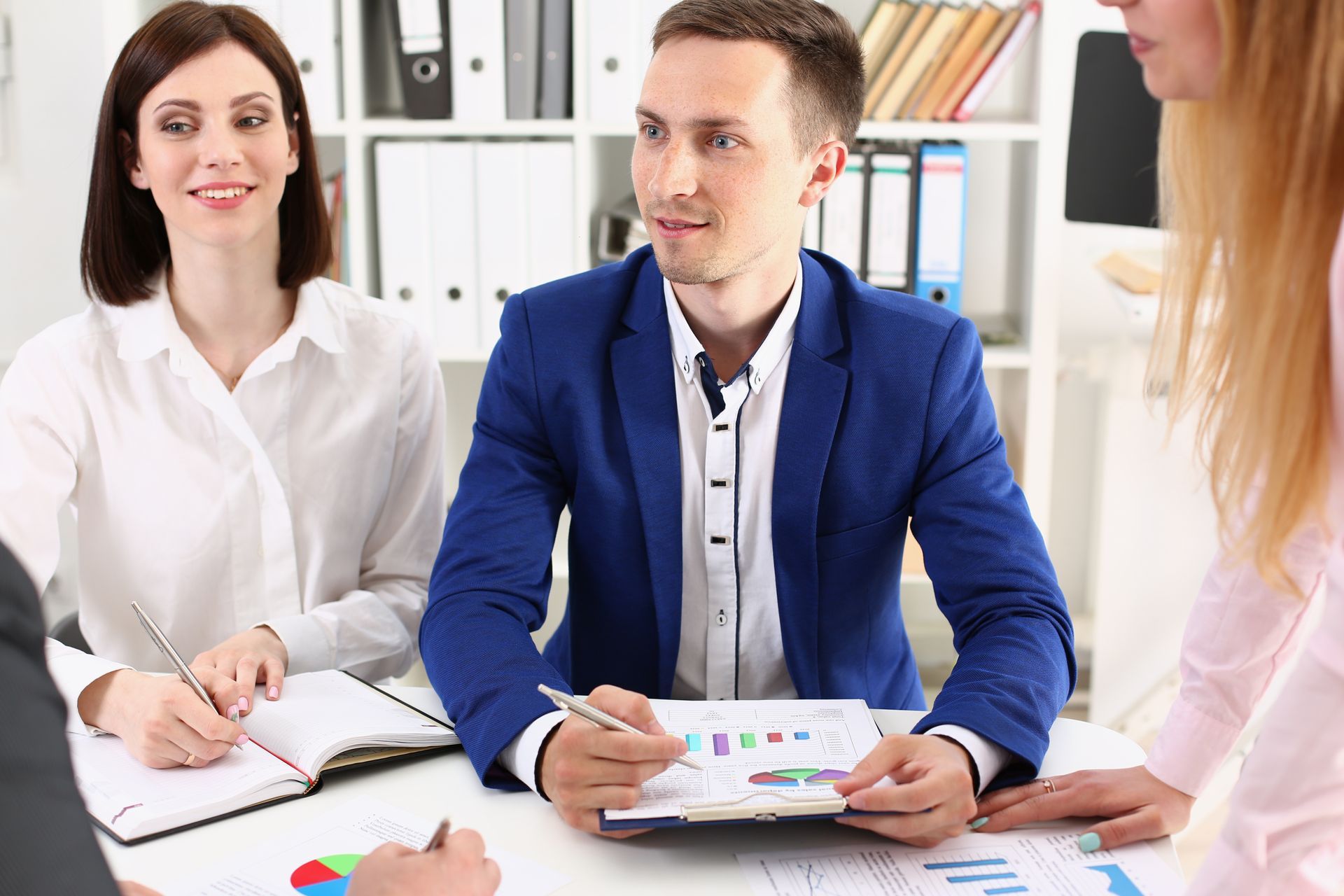 Colleagues in a bright office meeting, discussing charts and taking notes around a table