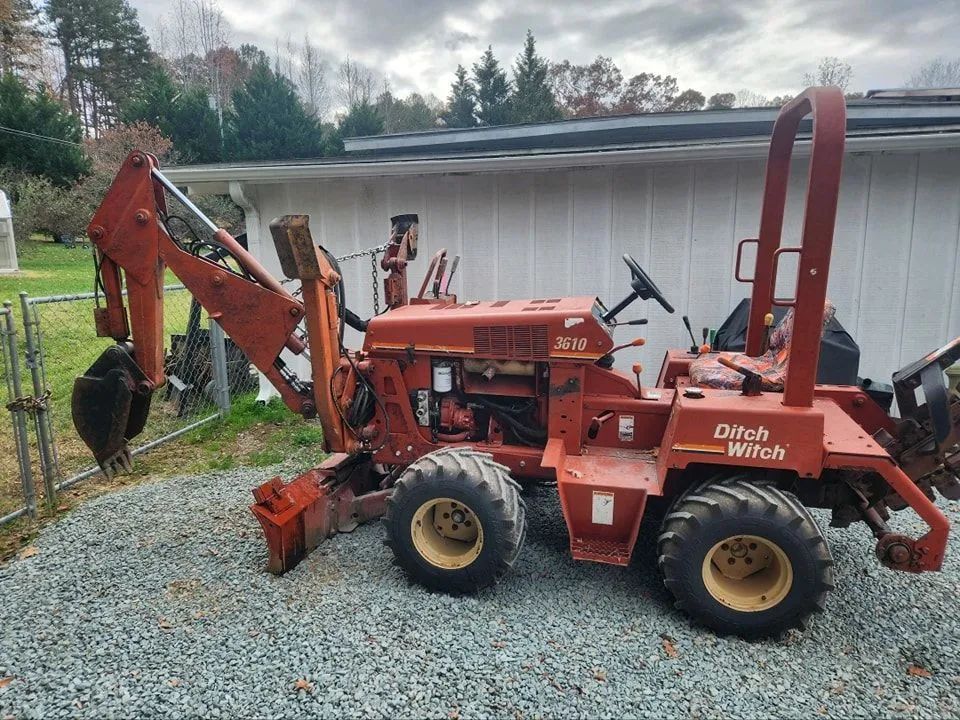 Red Kubota tractor with front loader and backhoe parked beside a white shed on gravel