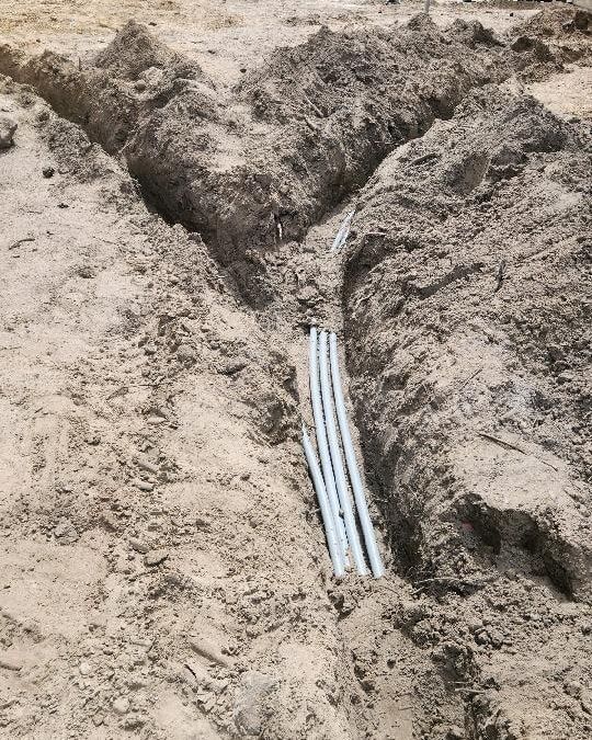 White pipes exposed in a dirt trench at a construction site.