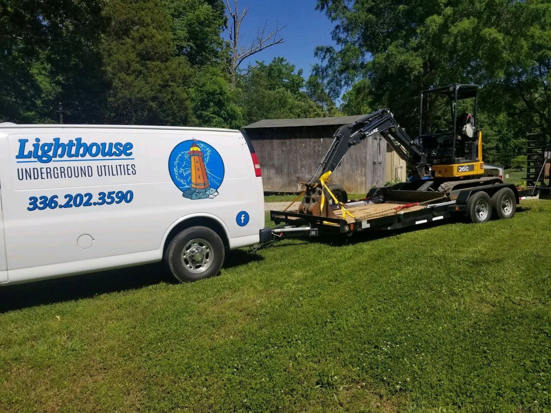 Lighthouse Unlimited Services van and trailer with excavator parked on a grassy lawn beside a shed