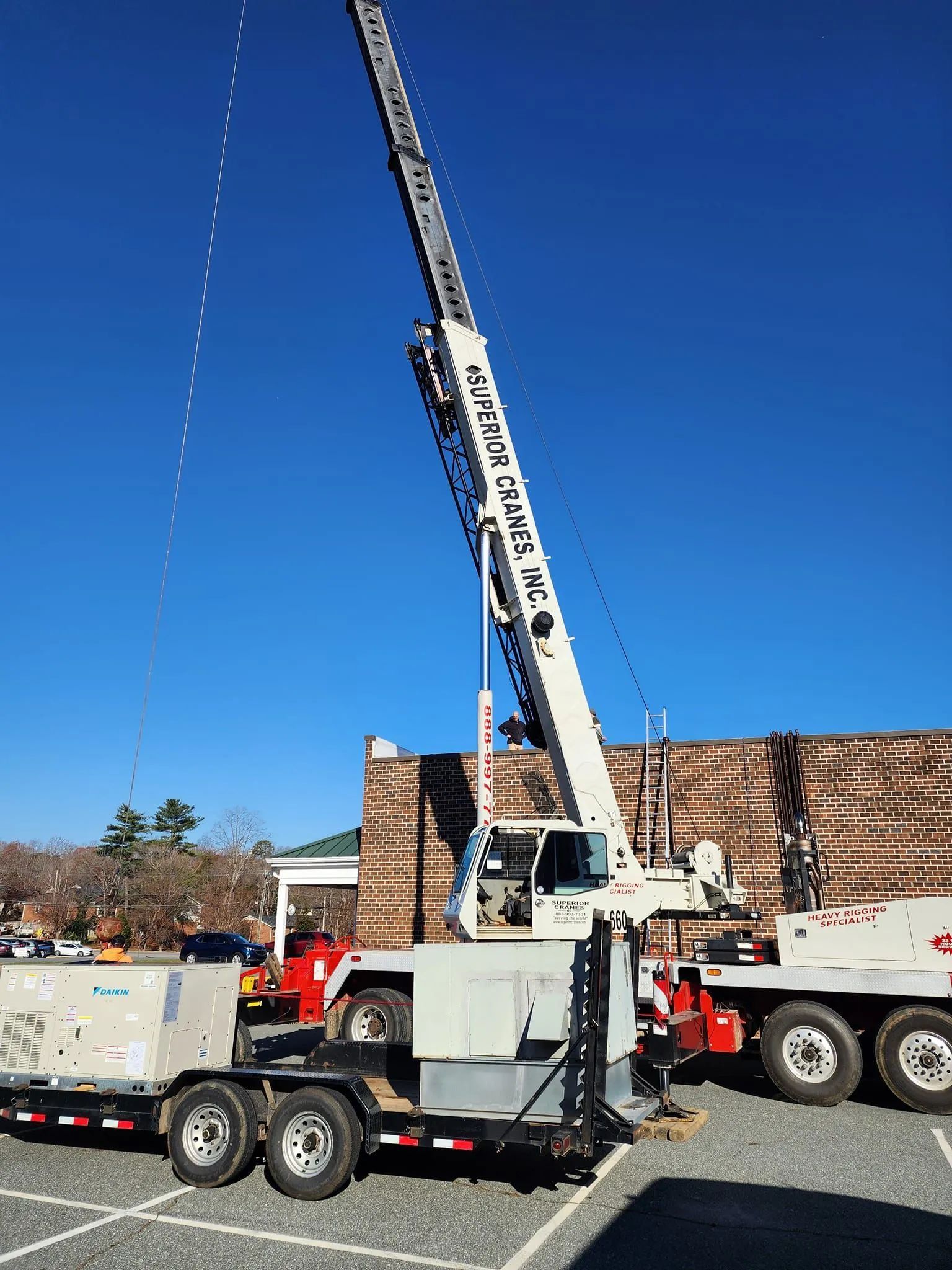 Tall white crane truck with boom raised beside utility trucks under a clear blue sky