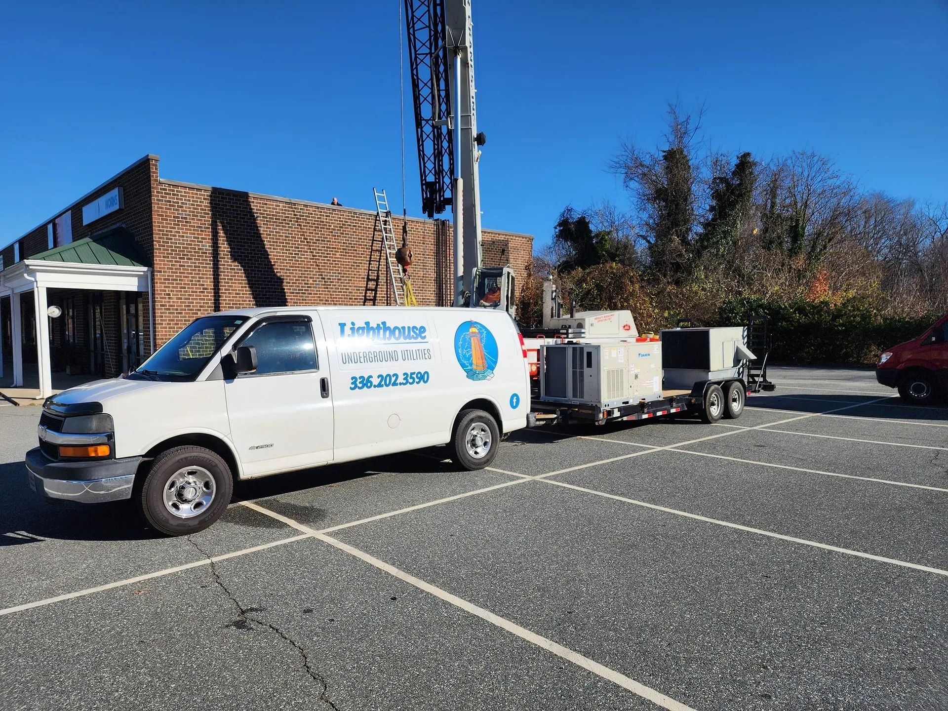 White service van with trailer parked in a lot beside a brick building under a clear blue sky