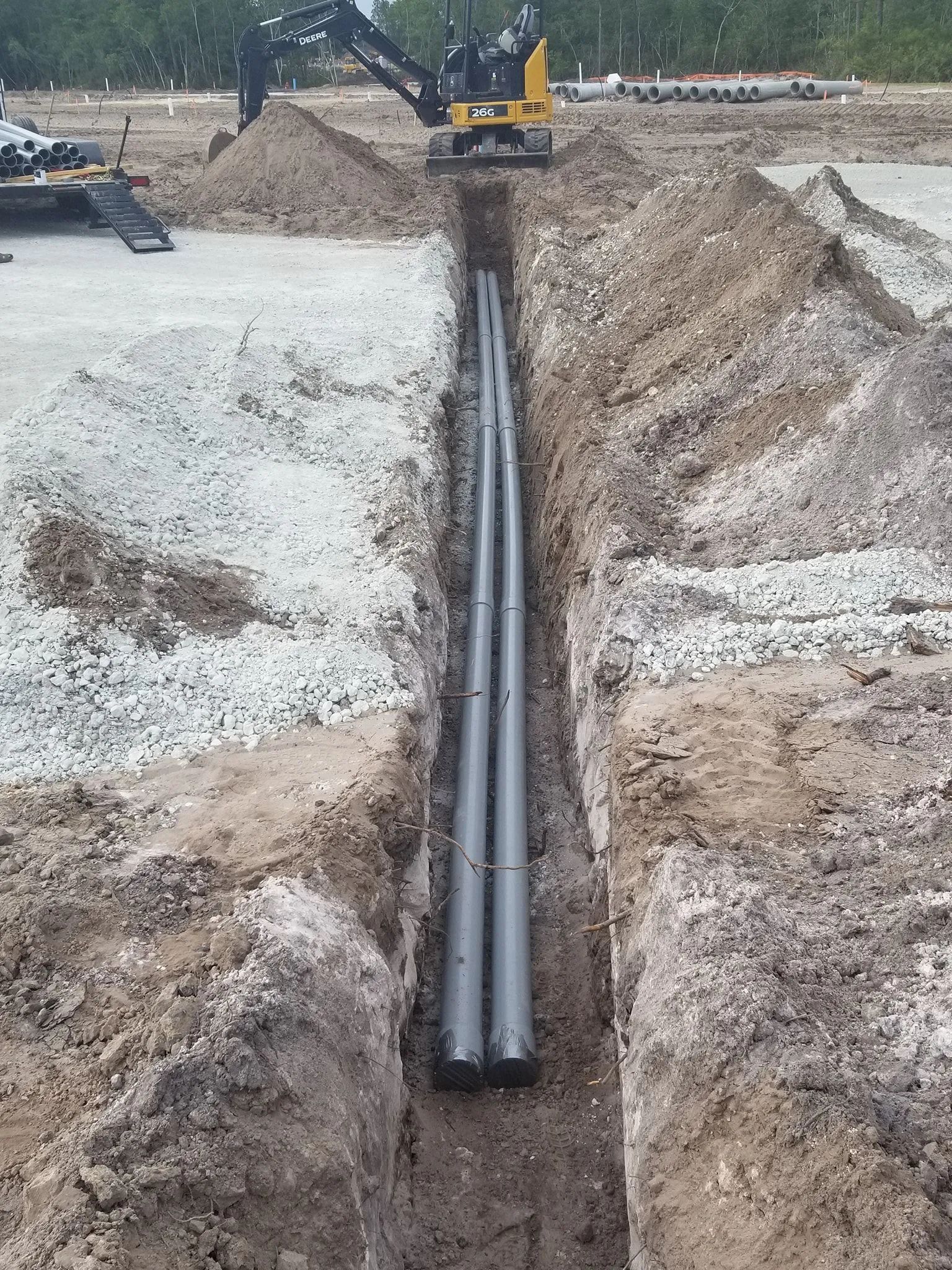 Construction trench with large pipes being laid underground by an excavator.
