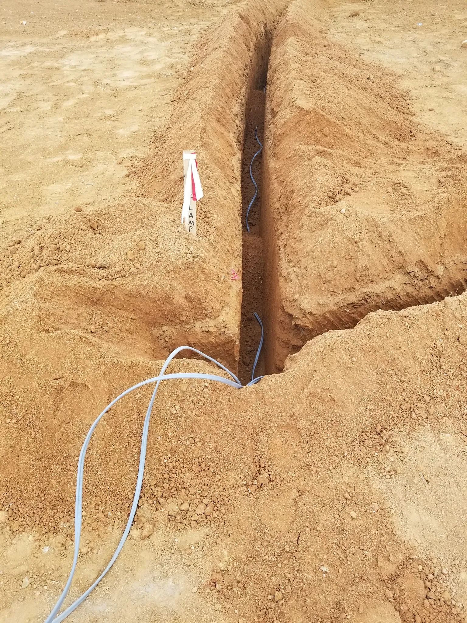 Shallow trench in sandy ground with exposed cables and a white marker flag.