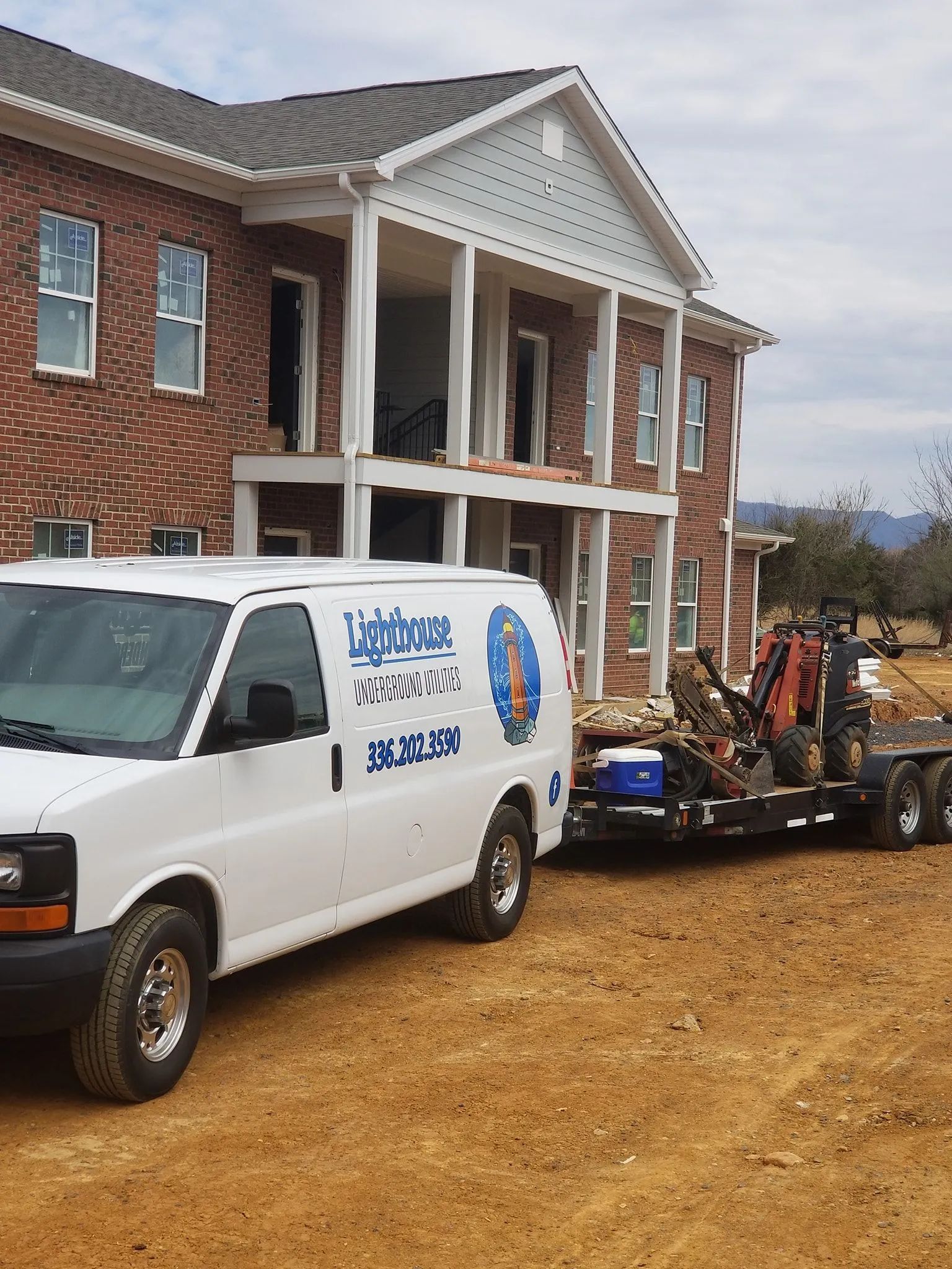 Construction equipment and a white work van parked beside a brick house under construction