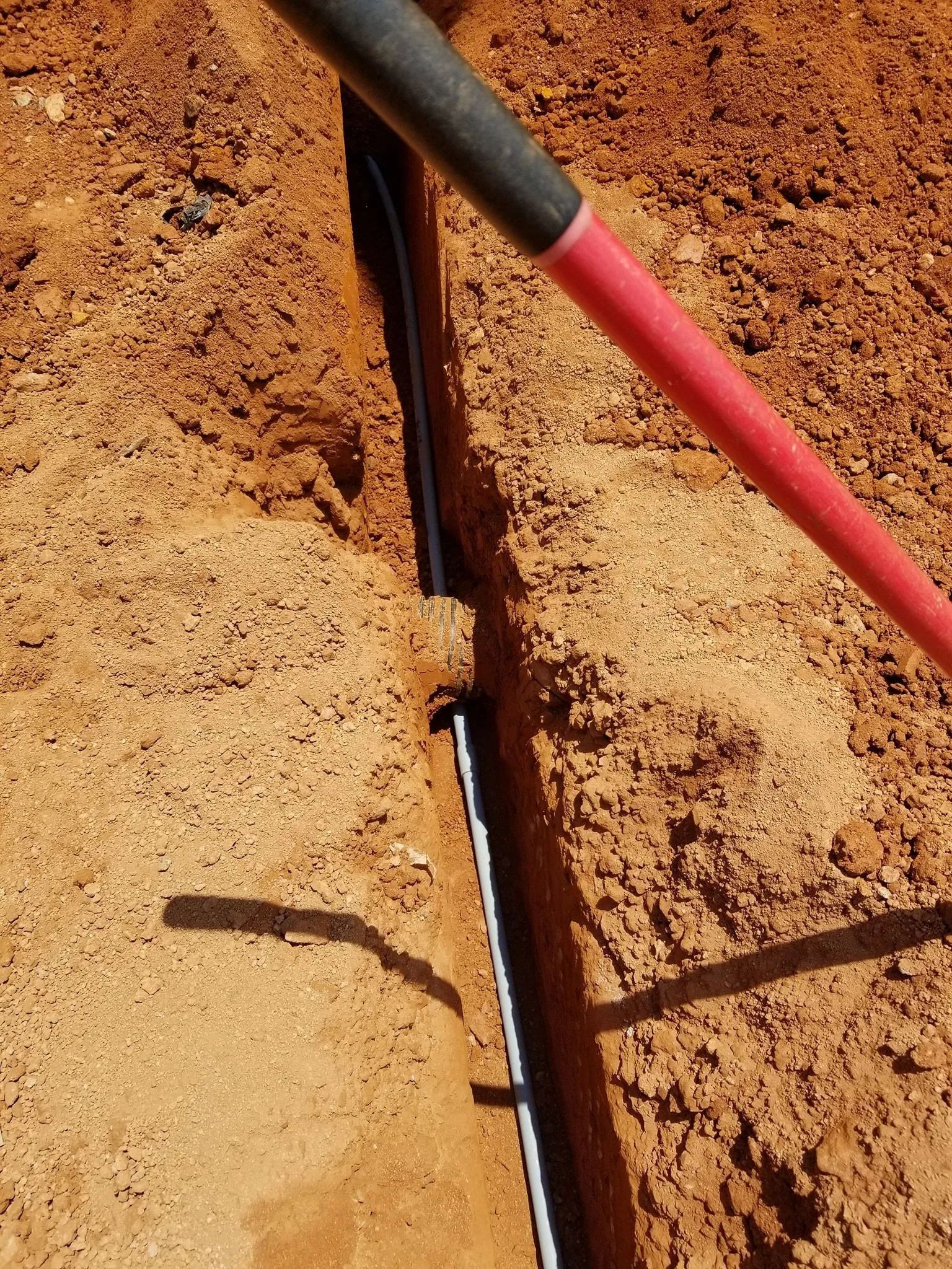 Red-handled tool in a narrow trench in dry brown soil