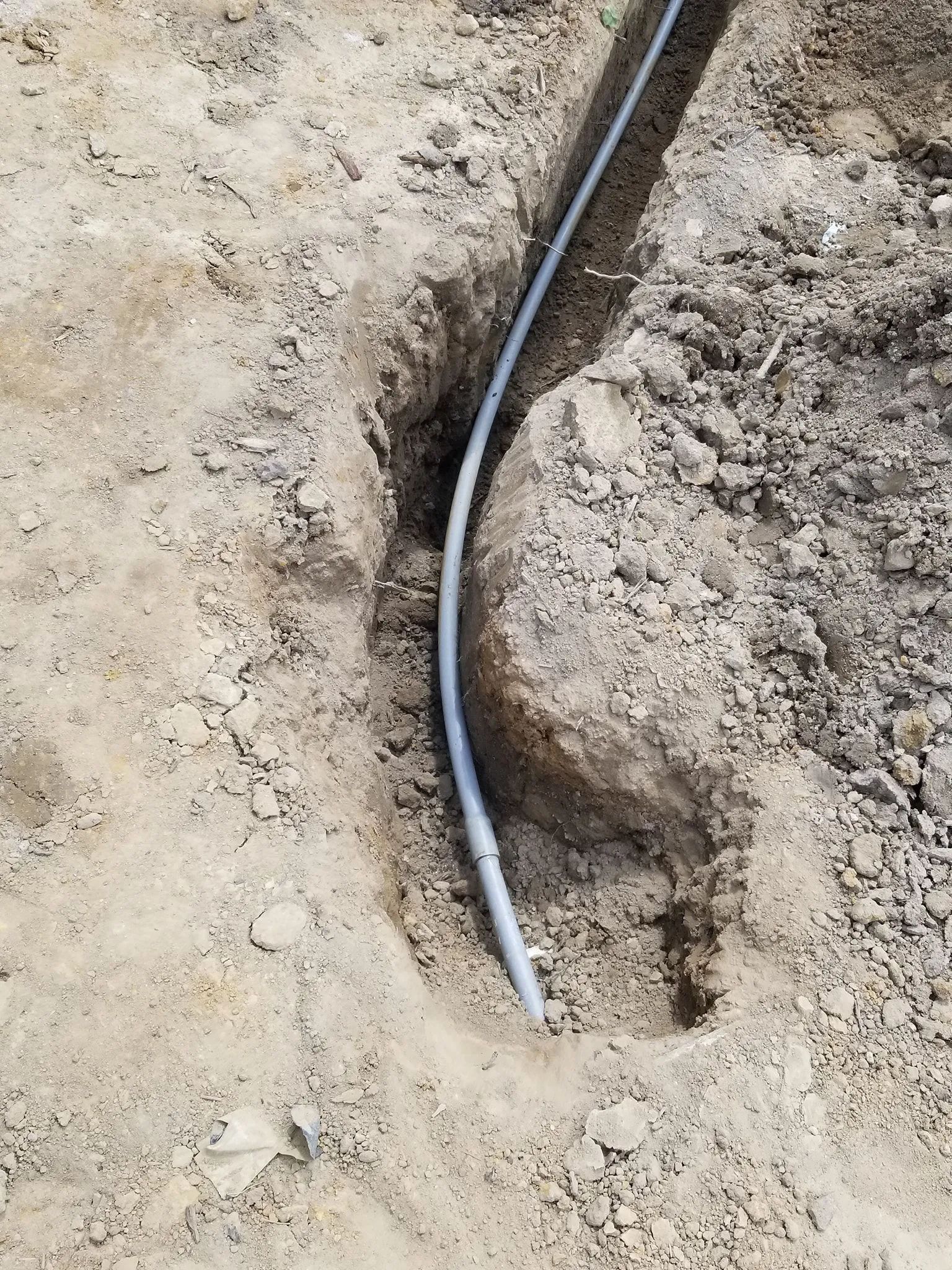 Black cable or pipe laid in a narrow dirt trench at a construction site