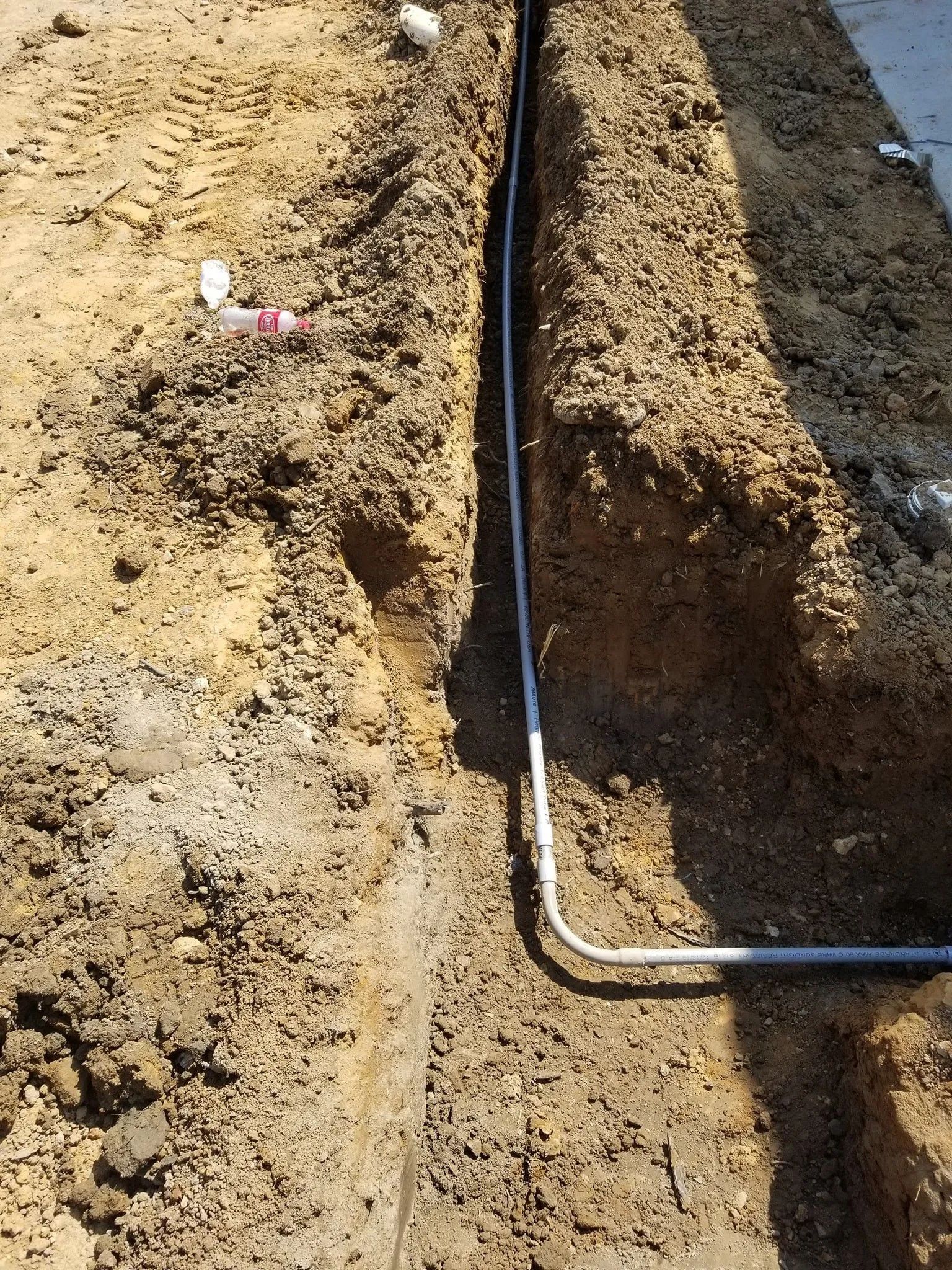 Trenched dirt path with a black cable and metal pipe running along the ground.