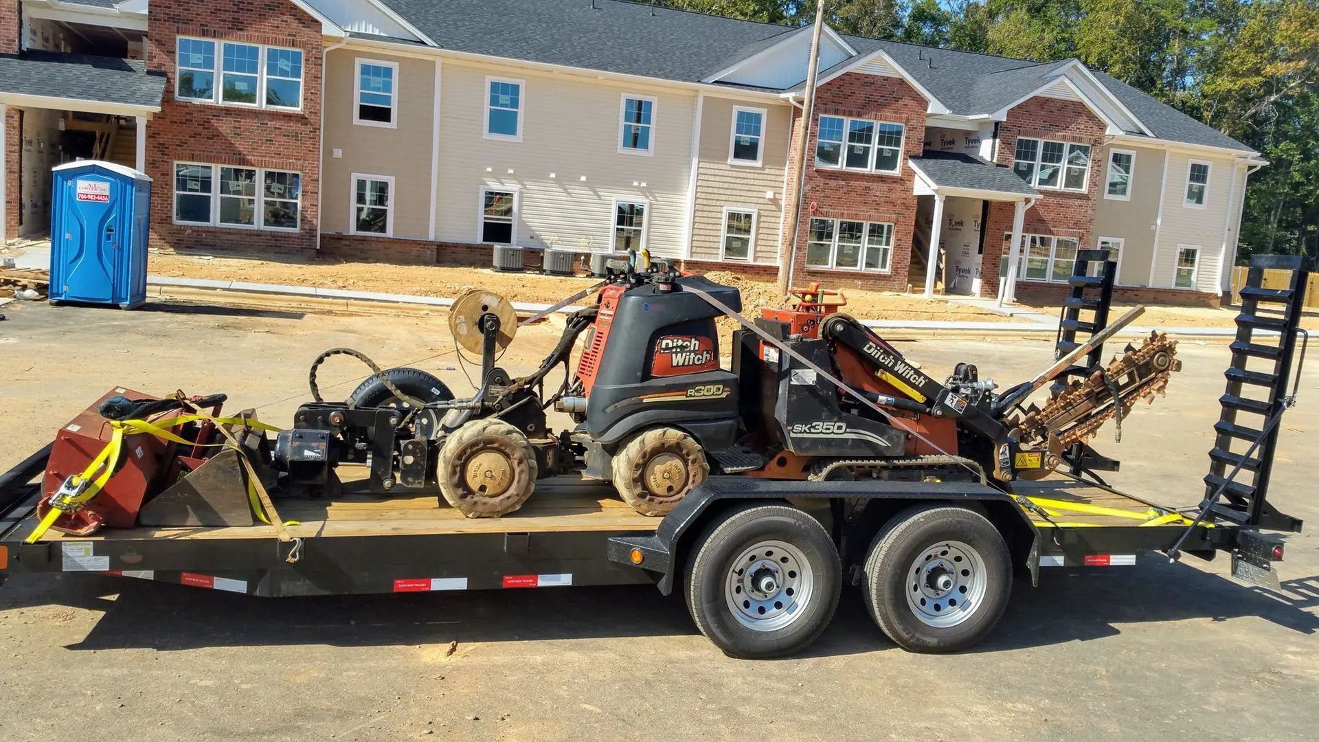 Black flatbed trailer loaded with lawn equipment parked in front of houses