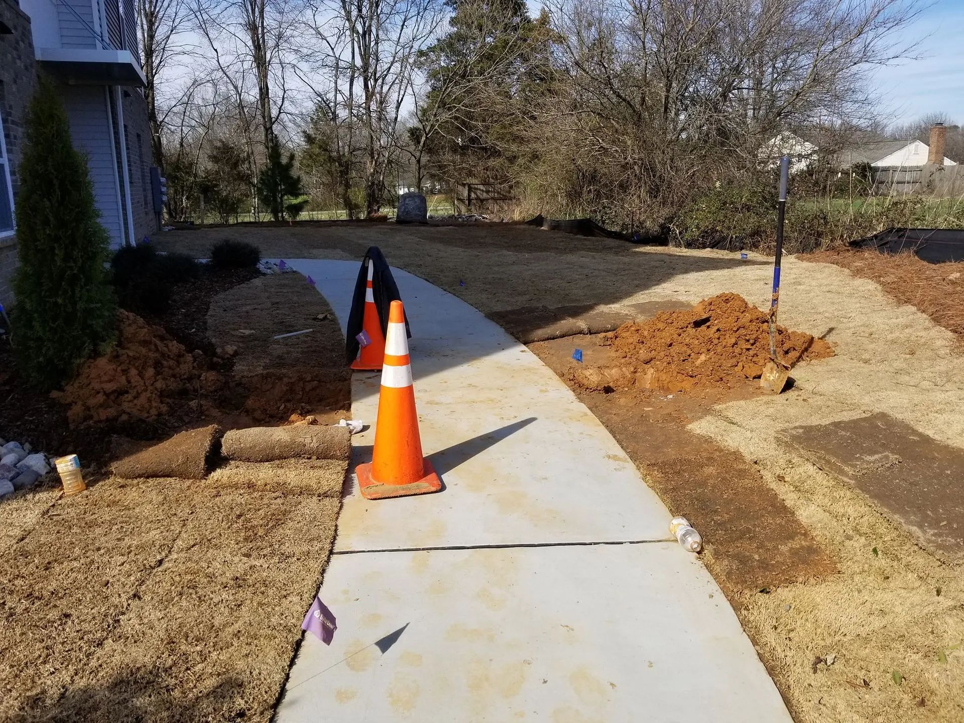 Sidewalk under construction with traffic cones beside a house and dirt landscaping area